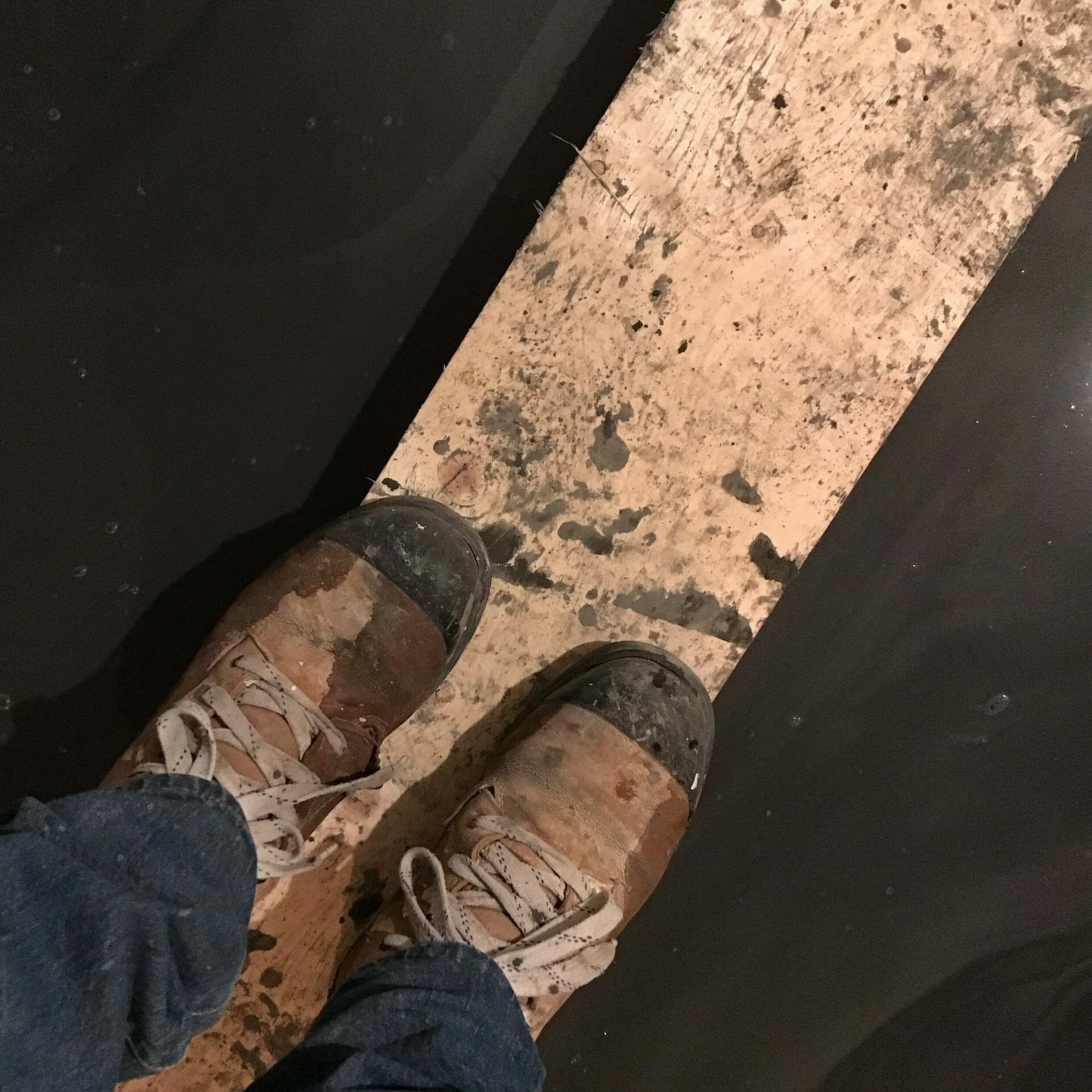 Work boots standing on plank over wet concrete.